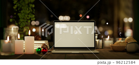 Workspace at night with laptop mockup with candles on wood table over blurred dark background. 96212584