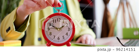 Businesswoman holding red alarm clock at workplace Businesswoman holding red alarm clock at workplace 96214151
