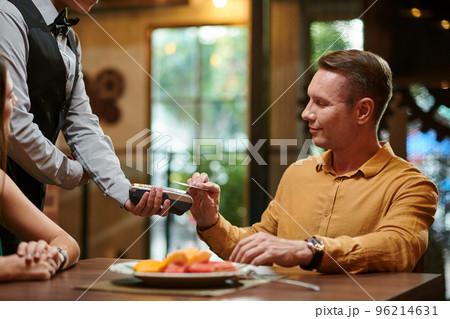 Smiling man paying for dinner in restaurant with credit card 96214631
