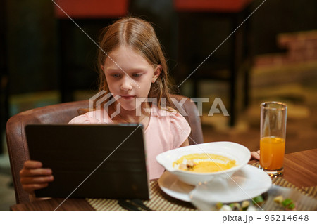 Preteen girl watching video on tablet computer when eating dinner in restaurant 96214648