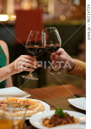 Cropped image of couple toasting with glasses or red wine over dinner table in restaurant 96214724