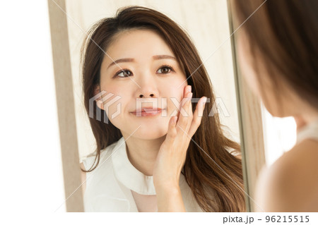 女性は鏡を見ながらスキンケアをしている。 女性は鏡を見ながらスキンケアをしている。 96215515