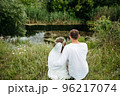A man hugs his beloved, sitting on the shore of a lake. 96217074