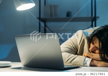 Late work. Tired man. Project deadline. Office guy in elegant suit falling asleep sitting desk opened laptop dark light room interior. Late work. Tired man. Project deadline. Office guy in elegant suit falling asleep sitting desk opened laptop dark light room interior. 96217801