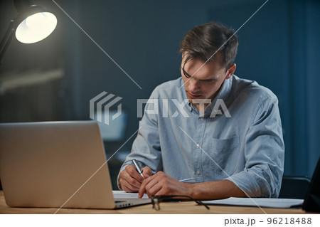 young businessman taking notes in his notebook during night work. young businessman taking notes in his notebook during night work. 96218488