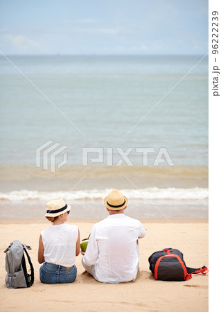 Couple with backpacks sitting on beach, drinking coconut cocktails and looking at waves Couple with backpacks sitting on beach, drinking coconut cocktails and looking at waves 96222239