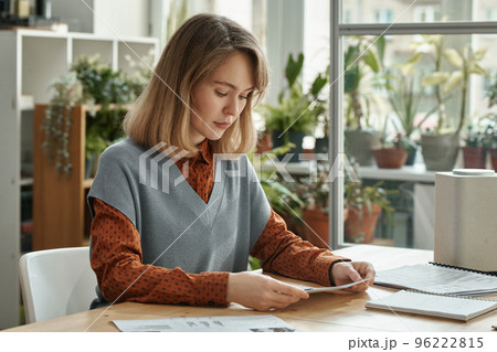 Young woman sitting at table and examining business documents working at light office with green plants Young woman sitting at table and examining business documents working at light office with green plants 96222815