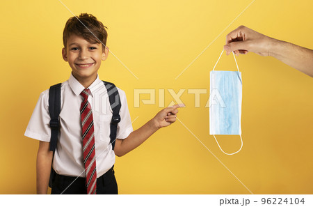 Young smiling student indicates a face mask for covid19. yellow background 96224104
