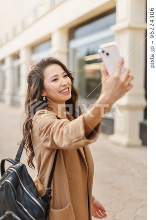 Asian kazakh female wearing beige coat, taking selfie, look at smartphone camera, walking on street Asian kazakh female wearing beige coat, taking selfie, look at smartphone camera, walking on street 96224306