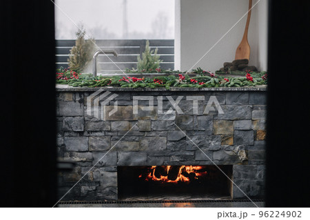 View from afar of steaming cast iron hot tub with spa in winter with snow and decorated candles. Christmas twigs with guelder rose and pine cones. View from afar of steaming cast iron hot tub with spa in winter with snow and decorated candles. Christmas twigs with guelder rose and pine cones. 96224902