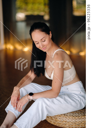 Portrait of a woman in white clothes sitting on an ottoman in the interior 96225336