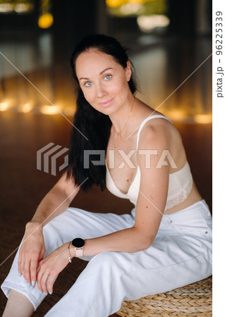 Portrait of a woman in white clothes sitting on an ottoman in the interior 96225339