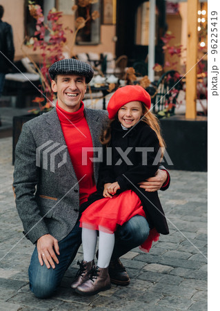 Portrait of a father and daughter sitting on a knee and being on a city street in autumn 96225419