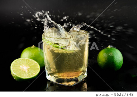 Shot of golden Mexican tequila with lime and salt on black background. A glass of tequila with lemon slices and splashing. Alcoholic drink concept. selective focus. 96227348