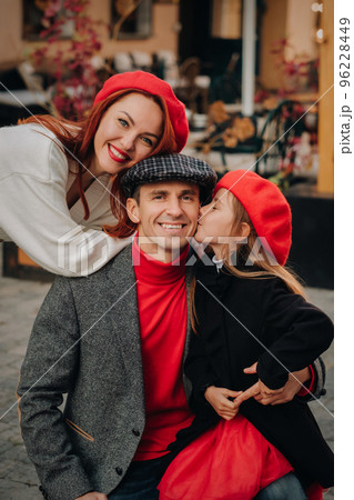 A stylish family of three strolls through the autumn city posing for a photographer . Dad, mom and daughter in the autumn city A stylish family of three strolls through the autumn city posing for a photographer . Dad, mom and daughter in the autumn city 96228449
