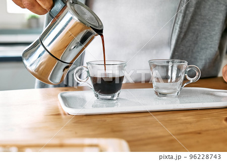 Man preparing classic Italian coffee in the mocha in the kitchen. Pouring coffee from moka pot into small glass coffee cup. Coffee brake. Morning habit. 96228743