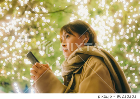 クリスマスの日に音楽を聴きながら待ち合わせをしている女性の写真 96230203