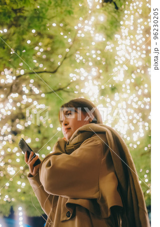 クリスマスの日に音楽を聴きながら待ち合わせをしている女性の写真 96230205