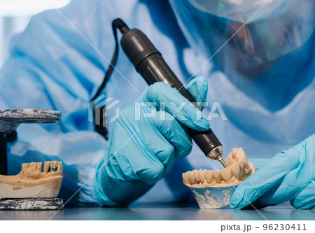 A masked and gloved dental technician works on a prosthetic tooth in his lab 96230411