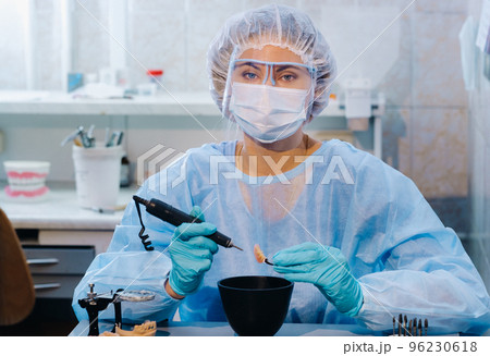 A dental technician in protective clothing is working on a prosthetic tooth in his laboratory 96230618