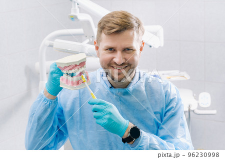 A model of a human jaw with teeth and a toothbrush in the dentist's hand 96230998