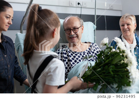 Sick grandfather receiving flowers from granddaughter in hospital room. Bedridden old man being visited by relatives in geriatric clinic room. Little girl giving flowers to bedridden elderly man. Sick grandfather receiving flowers from granddaughter in hospital room. Bedridden old man being visited by relatives in geriatric clinic room. Little girl giving flowers to bedridden elderly man. 96231495