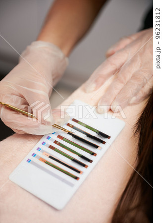 Close up of female hands in sterile gloves picking up volume lashes with stainless steel tweezers. Lash technician choosing eyelashes for lash extension procedure in beauty salon. Close up of female hands in sterile gloves picking up volume lashes with stainless steel tweezers. Lash technician choosing eyelashes for lash extension procedure in beauty salon. 96231812