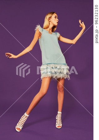 Image of pretty young blonde girl in blue cocktail dress dancing on purple background in studio Image of pretty young blonde girl in blue cocktail dress dancing on purple background in studio 96232130