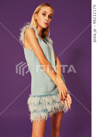 Image of cute beautiful slim blonde woman in elegant cocktail blue dress is posing at studio on purple background. Image of cute beautiful slim blonde woman in elegant cocktail blue dress is posing at studio on purple background. 96232170