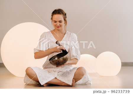 Portrait of a female yoga teacher playing a Tibetan bowl or singing a bell in the gym during a yoga retreat 96233739