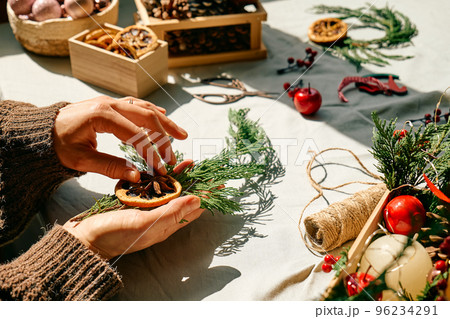 Woman making Christmas arrangement with fir branches and dried oranges. Female hands creating Christmas craft handmade decor. New year celebration. Winter holidays. Woman making Christmas arrangement with fir branches and dried oranges. Female hands creating Christmas craft handmade decor. New year celebration. Winter holidays. 96234291