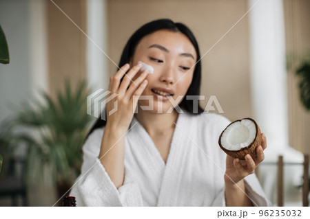 Close up view of face of young asian woman applying natural cosmetics at home Close up view of face of young asian woman applying natural cosmetics at home 96235032