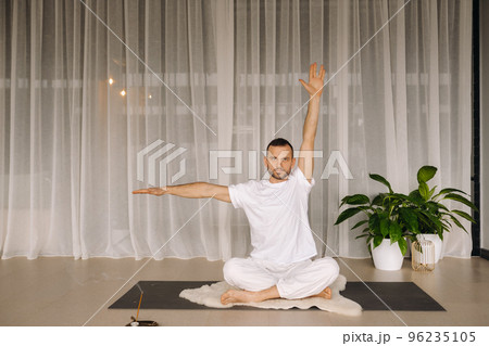a man in white sportswear is doing yoga with a fitness room. the concept of a healthy lifestyle a man in white sportswear is doing yoga with a fitness room. the concept of a healthy lifestyle 96235105