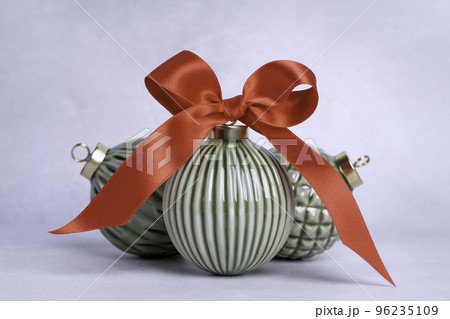 Green ceramic Christmas baubles with a red bow on a light background. Christmas decoration composition. Glossy decorative bulbs. Red ribbon bow tied on a retro style ceramic ball. 96235109