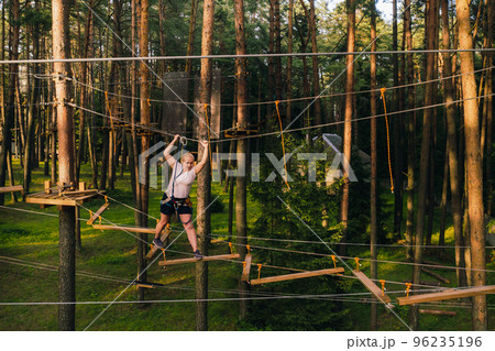 A woman overcomes an obstacle in a rope town. A woman in a forest rope park 96235196