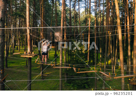 A woman overcomes an obstacle in a rope town. A woman in a forest rope park A woman overcomes an obstacle in a rope town. A woman in a forest rope park 96235201