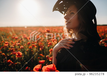 a girl in a black dress and hat on a poppy field at sunset 96235278