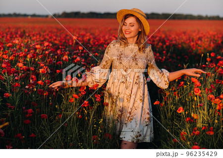 a girl in a dress, in a hat walks in a field with poppies at sunset 96235429