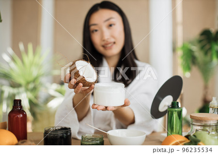 Focus on coconut and glass jar, young asian woman holding half of coconut and making homemade cream 96235534