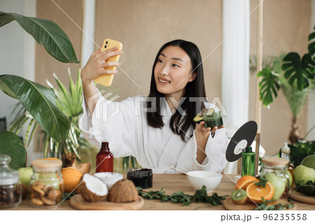 Asian brunette shoulder length hair female social media influencer holding glass jar with cream Asian brunette shoulder length hair female social media influencer holding glass jar with cream 96235558