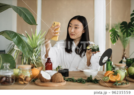 Asian brunette shoulder length hair female social media influencer holding glass jar with cream 96235559