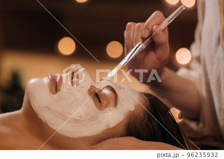 A cosmetologist makes a mask for a woman's face to rejuvenate the skin. Cosmetology 96235932