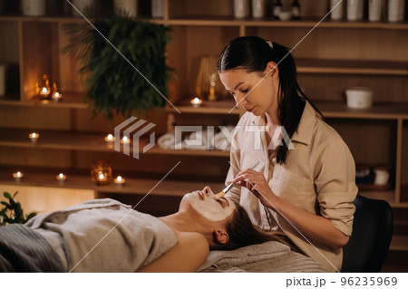 A cosmetologist makes a mask for a woman's face to rejuvenate the skin. Cosmetology 96235969