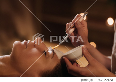 A cosmetologist makes a mask for a woman's face to rejuvenate the skin. Cosmetology A cosmetologist makes a mask for a woman's face to rejuvenate the skin. Cosmetology 96235978