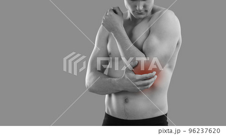 Muscular young man standing on gray background feels pain due to dislocation of elbow joint. Muscular young man standing on gray background feels pain due to dislocation of elbow joint. 96237620