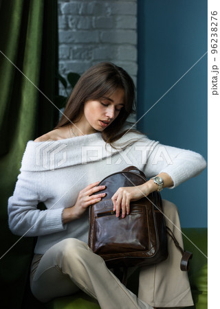 beautiful slender girl in beige pants and olive sweater posing while sitting on a green sofa with a small shiny brown leather backpack beautiful slender girl in beige pants and olive sweater posing while sitting on a green sofa with a small shiny brown leather backpack 96238276