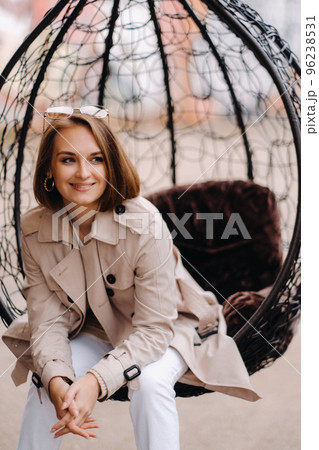 A happy stylish girl In a gray coat is sitting outside in an armchair 96238531
