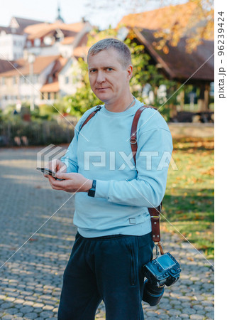 Professional Photographer Taking Picture Of Beautiful Autumn Park. Man Professional Photographer standing With Camera And With Smartphone In Autumn Park. Retouched, Vibrant Colors Professional Photographer Taking Picture Of Beautiful Autumn Park. Man Professional Photographer standing With Camera And With Smartphone In Autumn Park. Retouched, Vibrant Colors 96239424