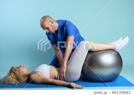 Girl performs exercises with a physiotherapist. Cyan background Girl performs exercises with a physiotherapist. Cyan background 96239682