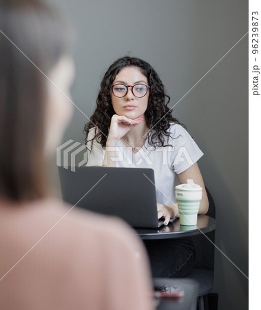 woman working in a coworking or coffee shop with a laptop and talking on the phone. spanish confident curly-haired woman  96239873